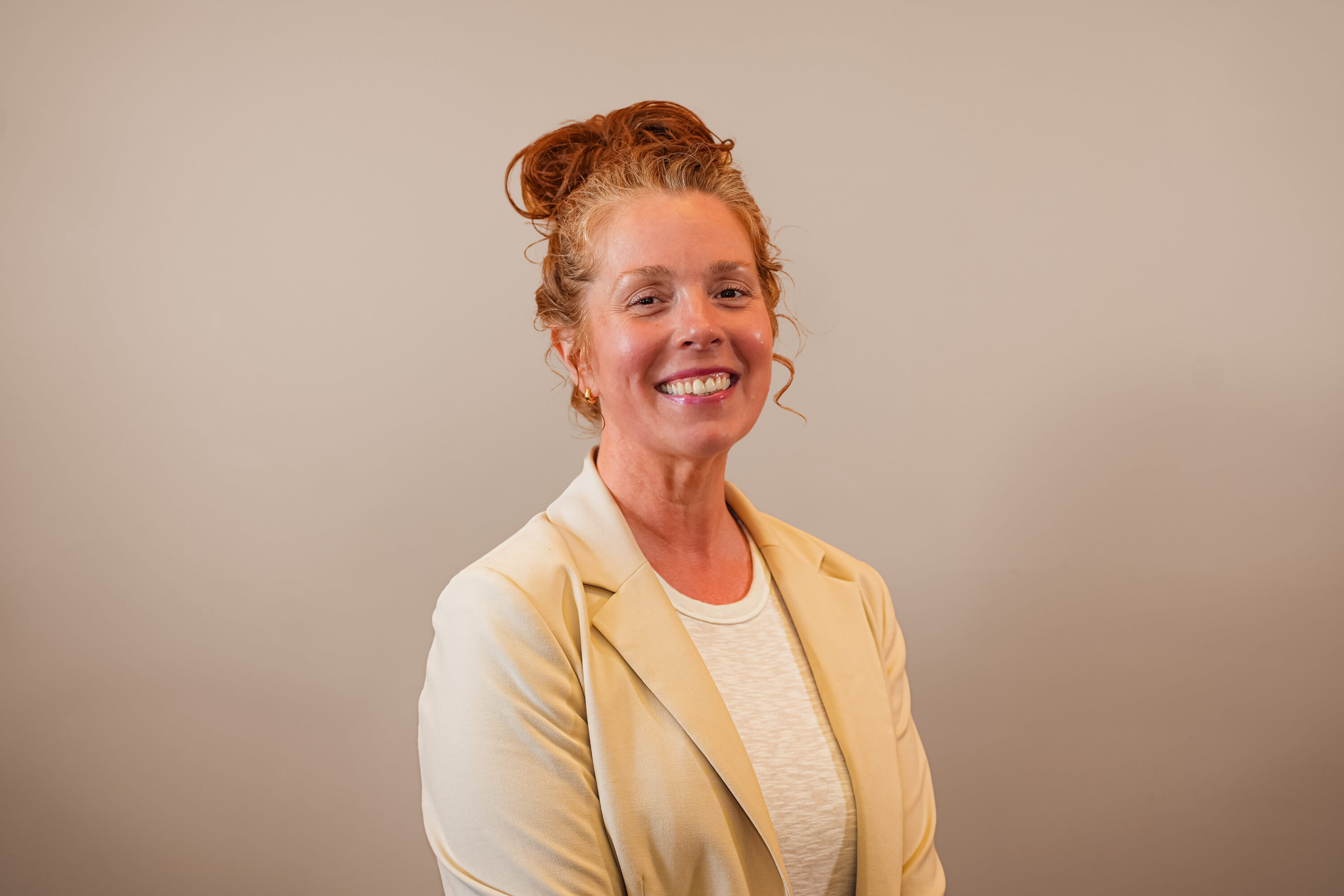 Smiling woman in beige blazer against neutral background
