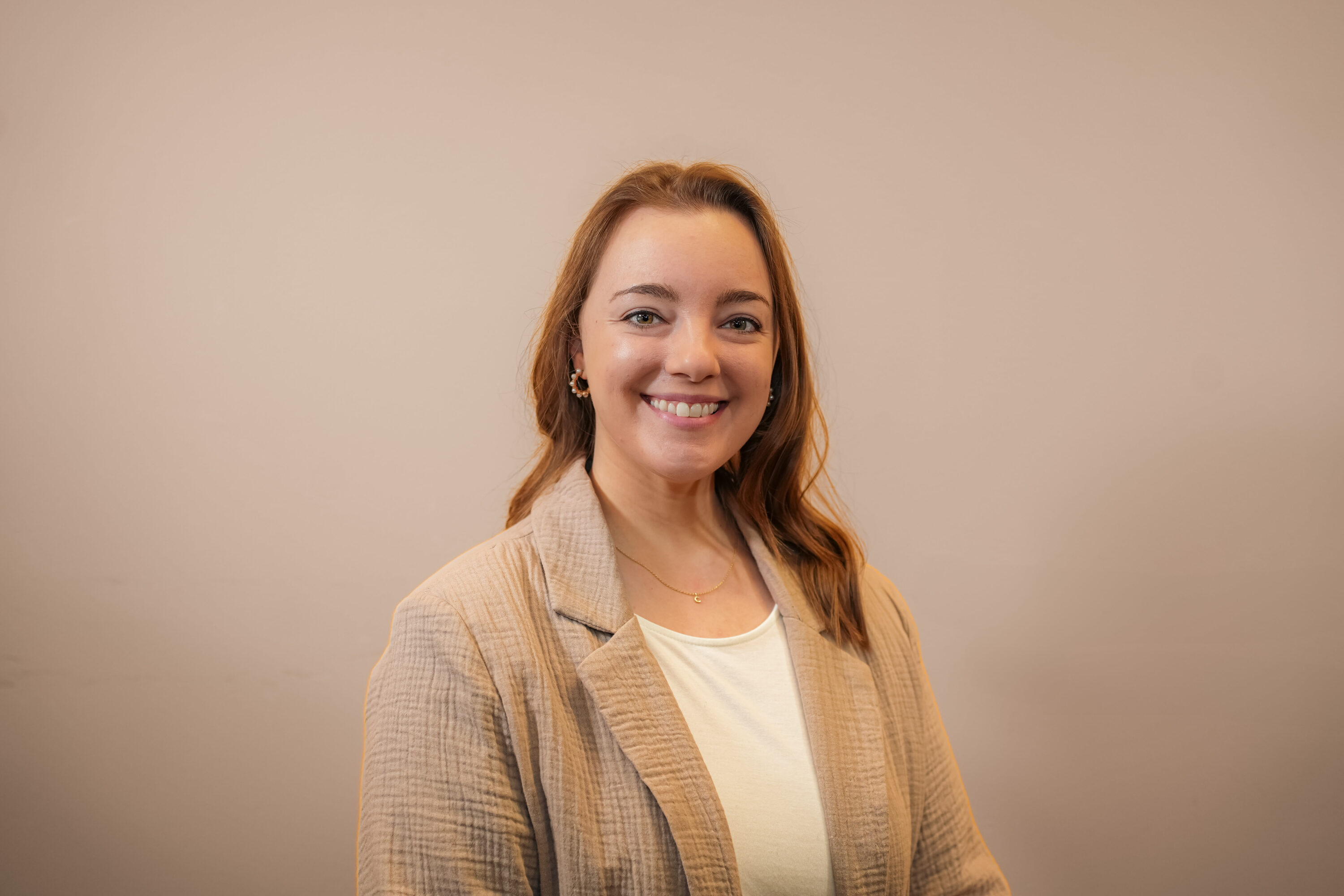 Smiling woman in beige blazer against neutral background