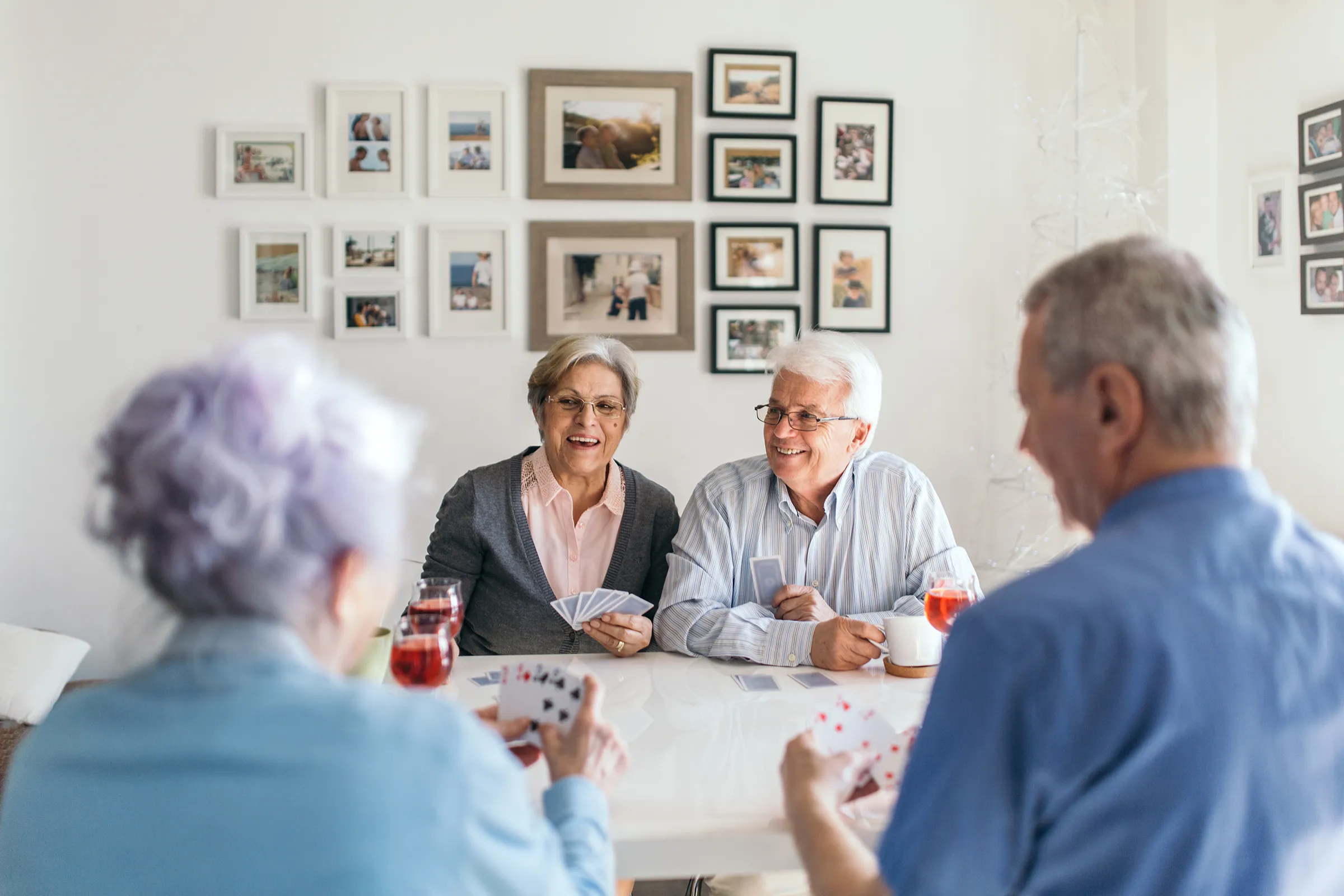 Four senior residents sitting around a table playing cards and socializing in a bright room with family photos on the wall at Keystone Villa at Fleetwood.