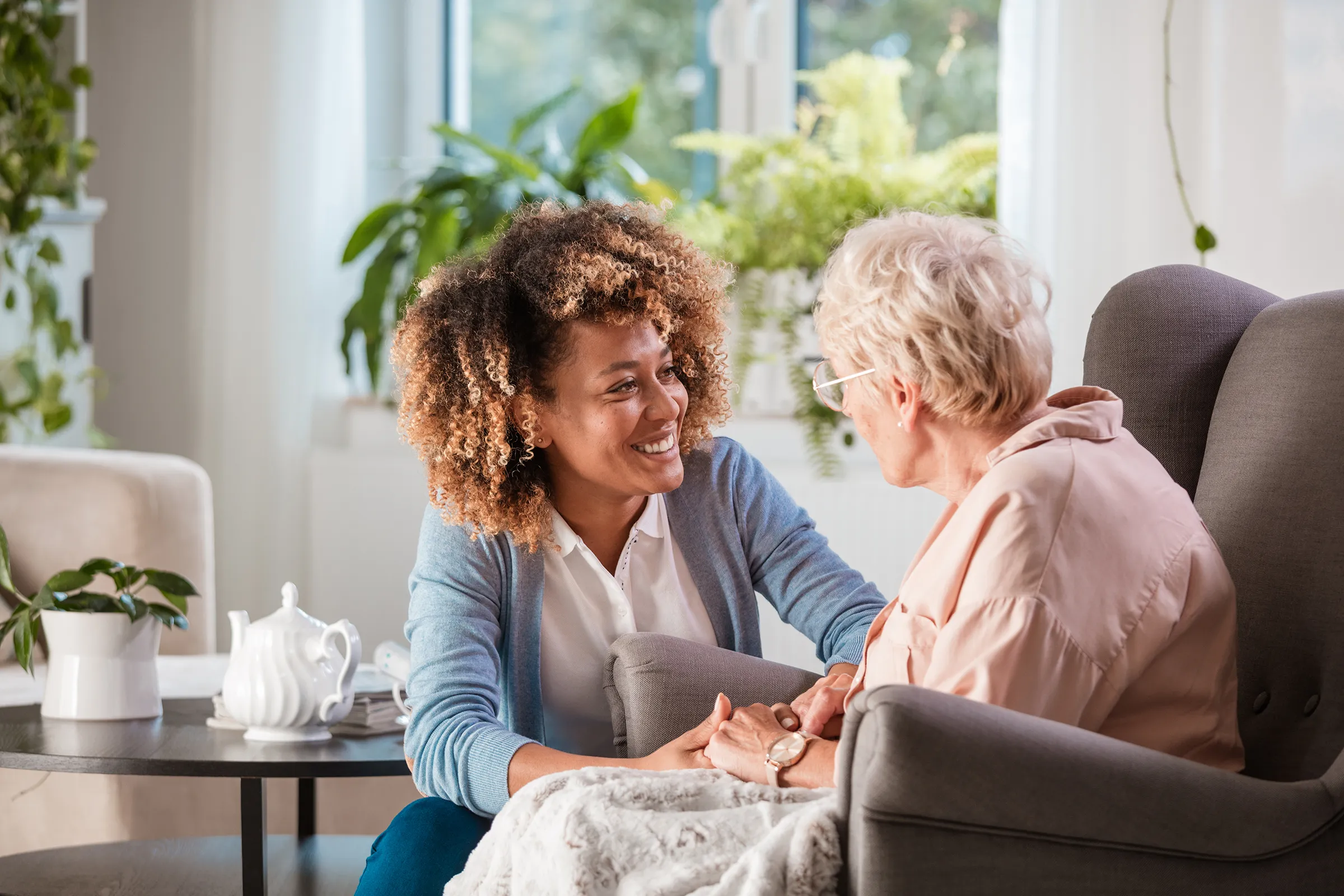 Caregiver holding elderly woman's hands in living room