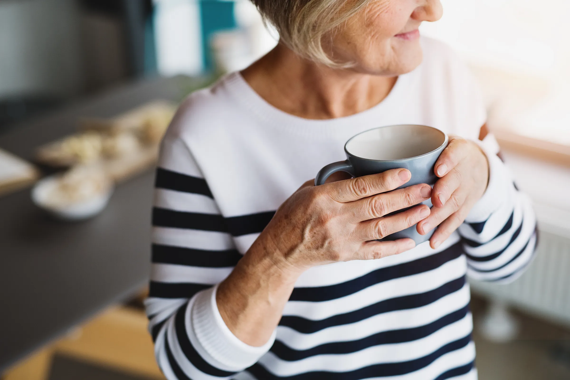 Older woman holding mug by window