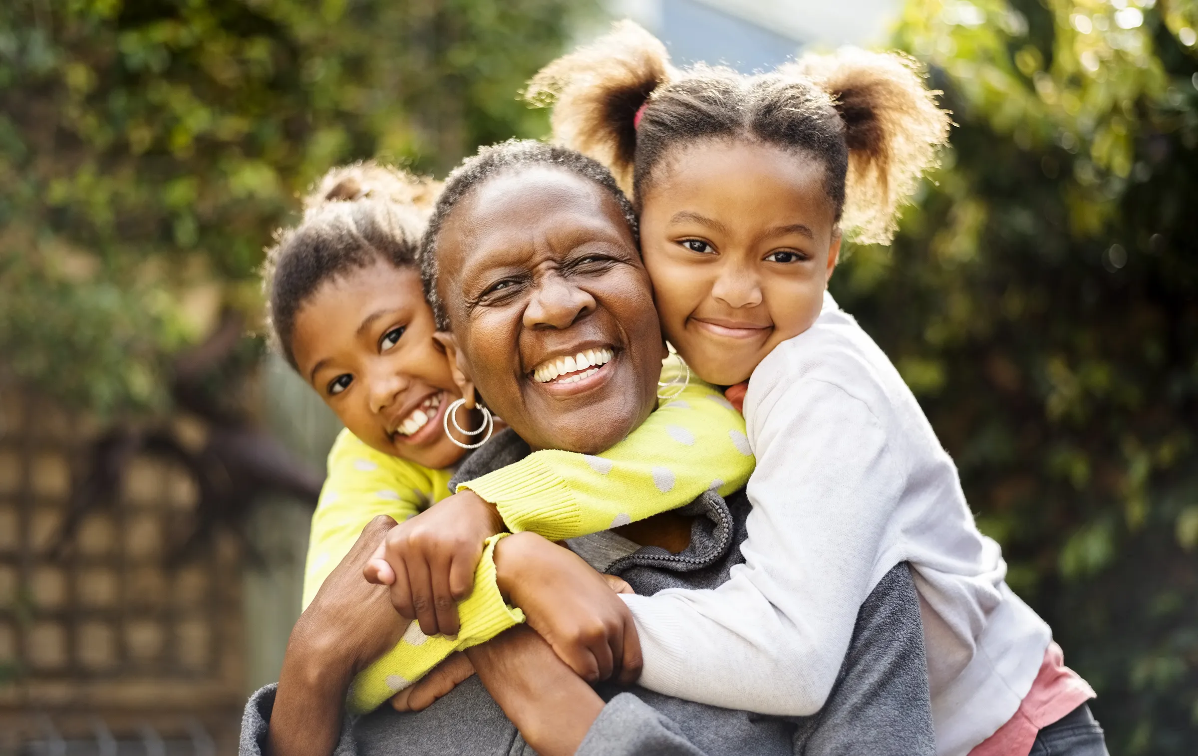 Grandmother hugging two smiling children outdoors