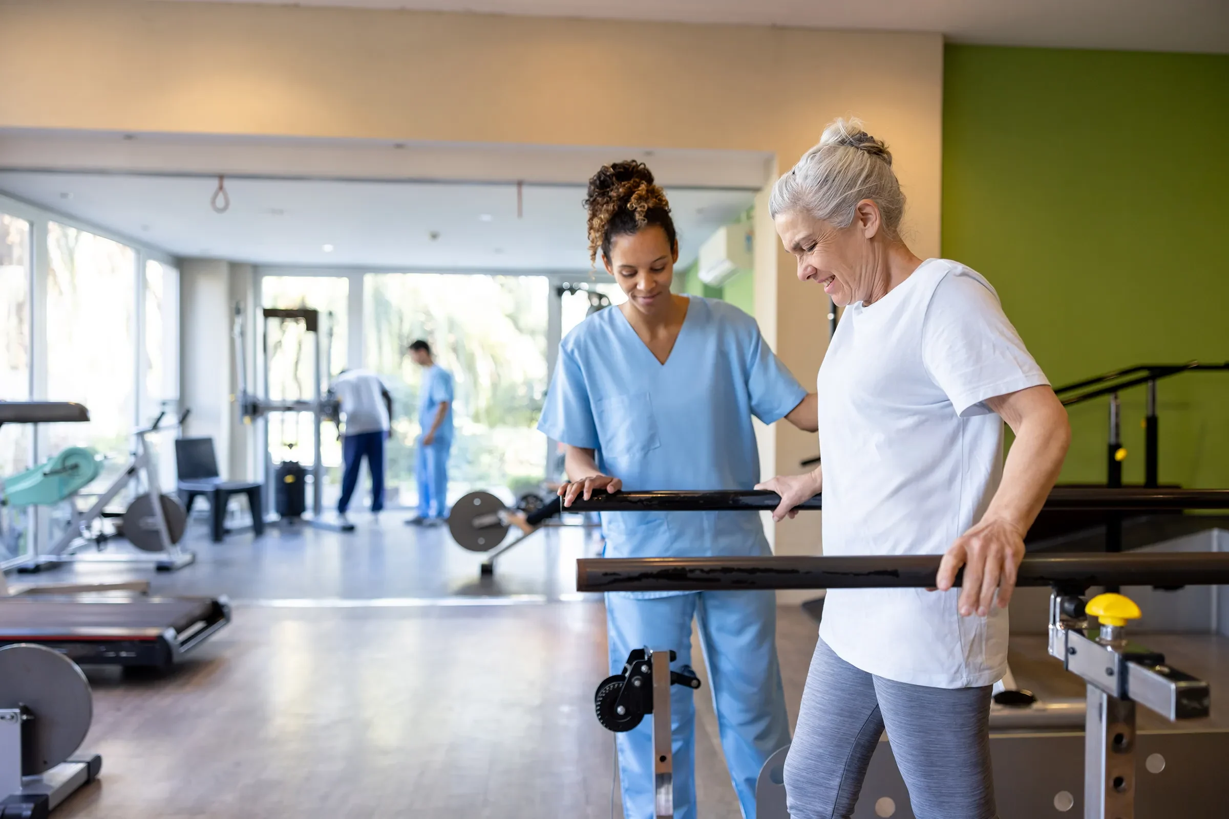 Physical therapist assisting senior woman with parallel bars