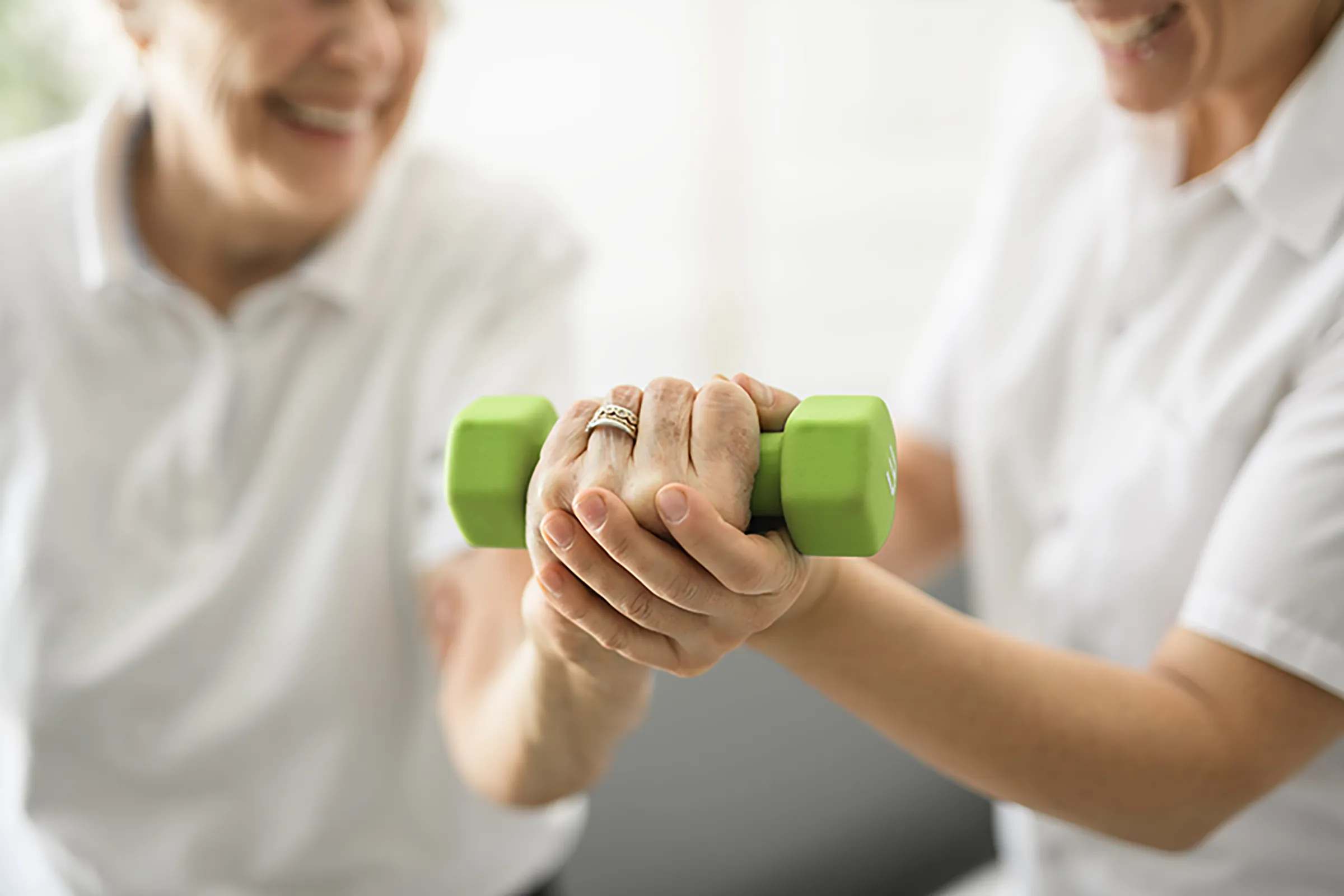 Caregiver assisting senior woman with dumbbell exercise