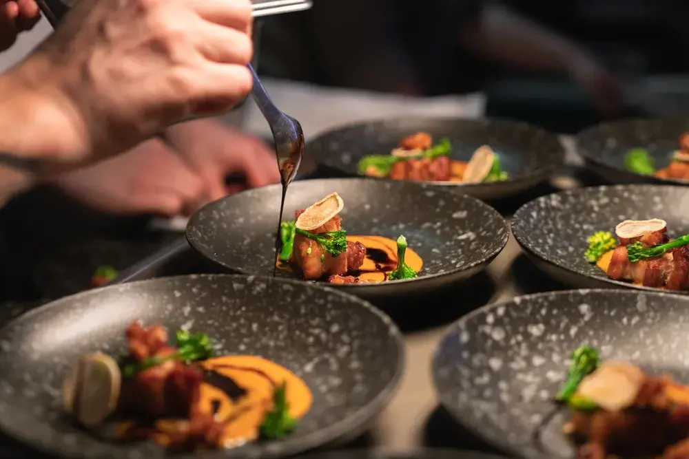 Hands plating gourmet meals on black dishes with sauce at Keystone Villa at Fleetwood dining service.